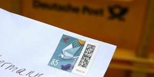 Ein Passant hält einen Brief mit einer 85-Cent-Briefmarke vor einen Briefkasten der Post.