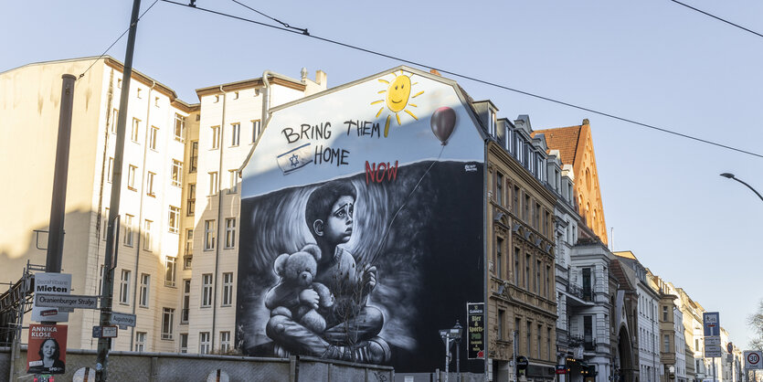 Eine riesige Wandmalerei an einer Brandmauer zweigt ein Kind mit einem Teddybären, darüber sind die Worte "Bring them home" zu lesen