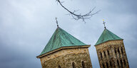 zwei schief stehende Kirchtürme vor dunklen Wolken