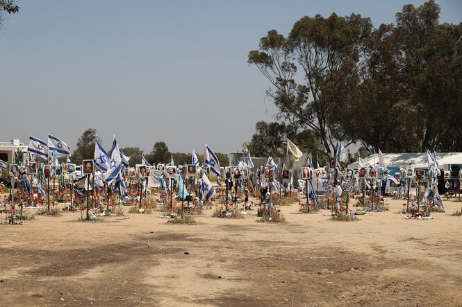 Israelische Fahnen und Fotografien stehen aufgereiht auf dem trockenen Boden eines Geländes