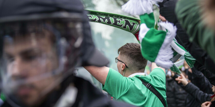 Ein Fan von Werder-Bremen, im Vordergrund steht ein Polizist