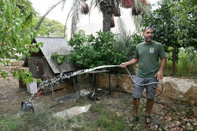 Eine Mann steht in einem Garten und gießt mit einem Wasserschlauch Pflanzen