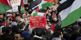 Demonstranten mit einem Schild auf dem steht: "From The River To The Sea"