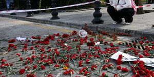 Eine Frau hockt neben niedergelegten Blumen für die Opfer in Ankara.