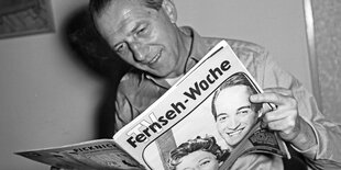 Eine Person hält eine Zeitung. Auf dem Titel steht: "Fernsehwoche"