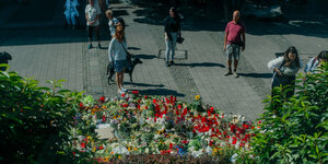 Menschen stehen vor einer Gedenkstelle aus Blumen