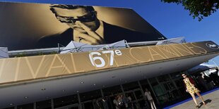 Menschen laufen an einer großen Leinwand vorbei, die auf das Cannes-Festival hinweist.