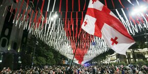 Demonstranten stehen mit georgischer Flagge im Freien.