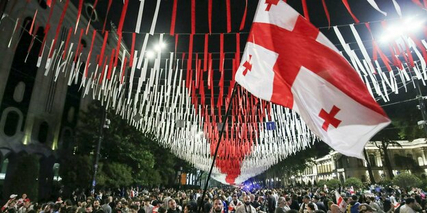 Demonstranten stehen mit georgischer Flagge im Freien.