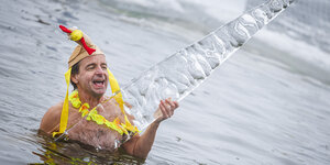 Ein Mann mit Hühnermütze beim Eisbaden mit einem riesen Eiszapfen in der Hand