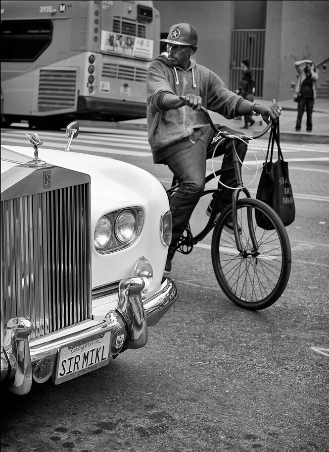 A person on a Fahrrad drives a Luxus car.