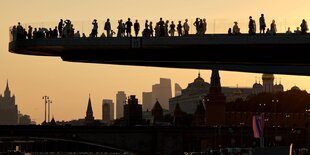 Menschen stehen in Moskau auf einer Aussichtsbrücke im Sonnenuntergang