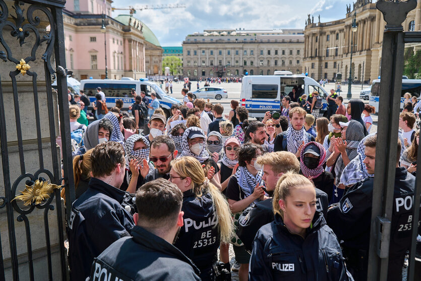 Eine por-palästinensische Demonstration. Viele Menschewn stehen vor einem tor. Im Tor stehen Polizist*innen. Hiter den Menschen auf der Straße stehen Polizeiwagen.