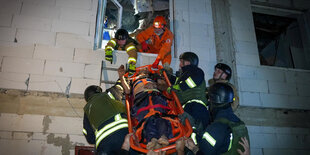 Eine Rettungsbahre mit einem Menschen wird aus einem Fenster geschoben und von Rettungskräfnten aufgenommen