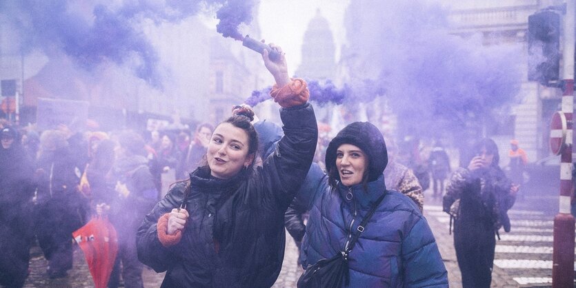 Zwei Frauen halten Pyrotechnik in den Händen, sie stehen in lilafarbenem Rauch