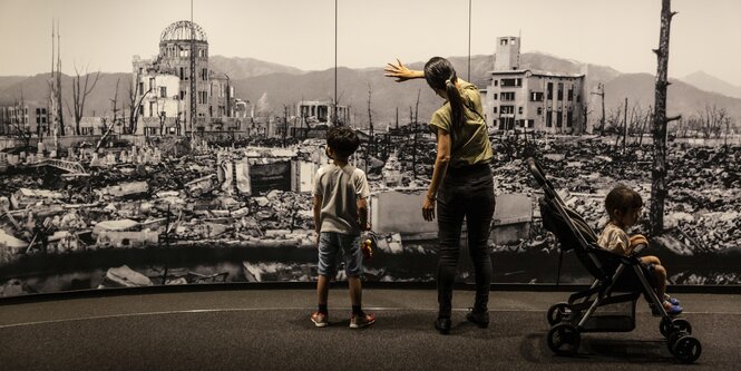 Eine Frau mit zwei kleinen Kindern schaut auf ein Panorama von Hiroshima nach dem Bombenabwurf