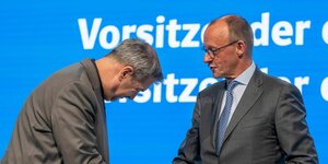 Markus Söder verbeugt sich vor Friedrich Merz. Sie reichen sich dabei die Hand.