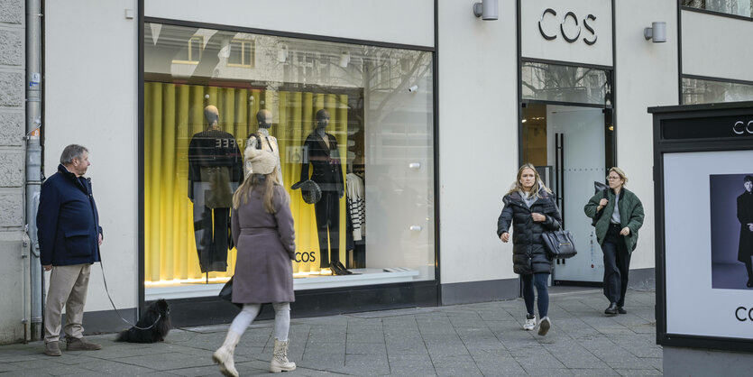 Ein Geschäft mit Mode im Schaufenster, davor Passanten. Es ist eine Filiale der Bekleidungskette "COS"