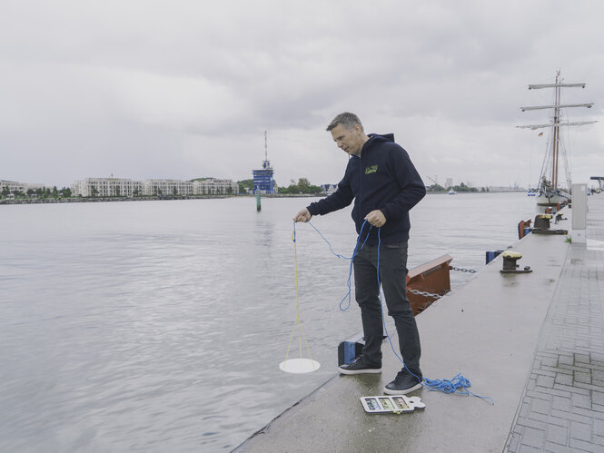 Prof. Dr. Oliver Zielinski steht an einem Kaisteg und misst mit der Secci-Scheibe, wie viel Licht ins Wasser fällt