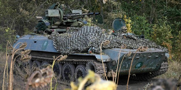 Ein Panzer steht im Dickicht, zwei Soldaten schaut aus der Luke und auf dem vorderen Teil liegt ein Tarnnetz