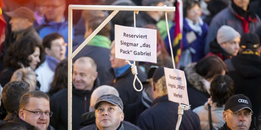 Menschen nebeneinander, irgendwer hält einen Galgen, an dem zwei Schilder hängen, dass dieser für Angela Merkel und Sigmar Gabriel gedacht ist