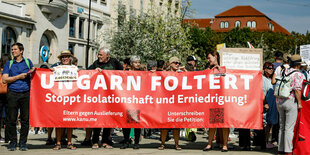 Menschen demonstrieren in Erfurt, sie tragen ein großes rotes Banner vor sich auf dem steht: Ungarn foltert, Stoppt Isolationshaft und Erniedrigung !