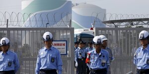 Polizisten in Uniform stehen vor einem abgeriegelten Gelände eines Atomkraftwerks in Japan