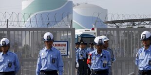 Polizisten in Uniform stehen vor einem abgeriegelten Gelände eines Atomkraftwerks in Japan