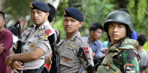 Drei Sicherheitskräfte stehen bei einem Tatort einer niedergebrannten Kirche in Indonesien