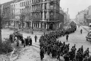 Ein schwarz-weiß-Foto aus dem Oktober 1944 zeigt eine Kolonne deutscher Kriegsgefangener in Aachen, bewacht durch US-Soldaten