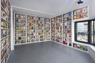 Bücherregale füllen einen Ausstellungsraum. Sie reichen bis unter die Decke uns sind mit bunten, fotografierten Buchcovern gefüllt