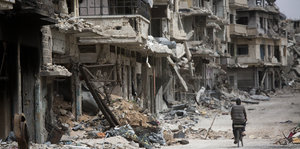 Ein Radfahrer durchfährt einen zerstörten Teil der syrischen Stadt Homs.