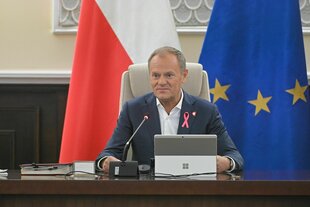 Donald Tusk sitzt an seinem Schreibtisch, hinter ihm die europäische und polnische Flagge