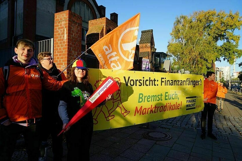 Aktivisten mit Schultüten und Flagge von Attac stehen vor einem Banner mit der Aufschirft: Vorsicht: Finanzfänger ! Bremst euch Marktradikale