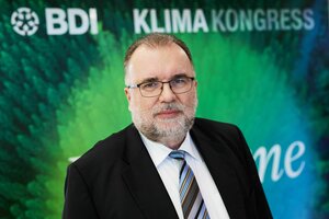 Porträt von Siegfried Russwurm vor einer grünen Wand mit dem Logo des BDI und Klimakongress, er trägt Bart, Brille, Krawatte -sehr seriös