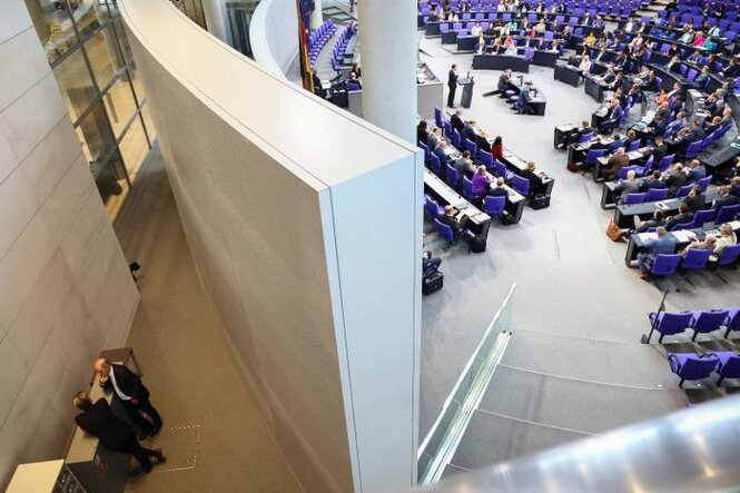 Blick in den Bundestag. Hinter einer Wand sieht man Olaf Scholz im Gespräch mit einer Person.