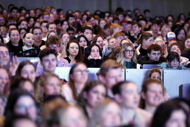 Student*innen sitzen in den Bänken eines großen Hörsaals und lauschen einem Vortrag