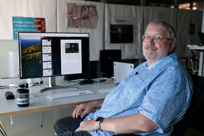 Ein Mann, Ralf Klever, sitzt in einem Bürostuhl vor einem Schreibtisch, auf dem Schreibtisch steht ein Monitor, der Seiten des taz-ePapers zeigt