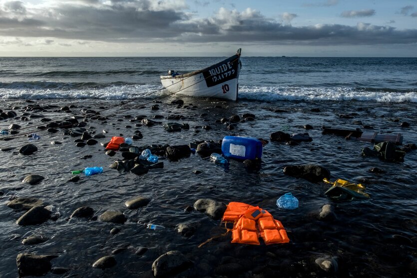 Schwimmwesten und Gepäckstücke im Meer vor einem Holzboot