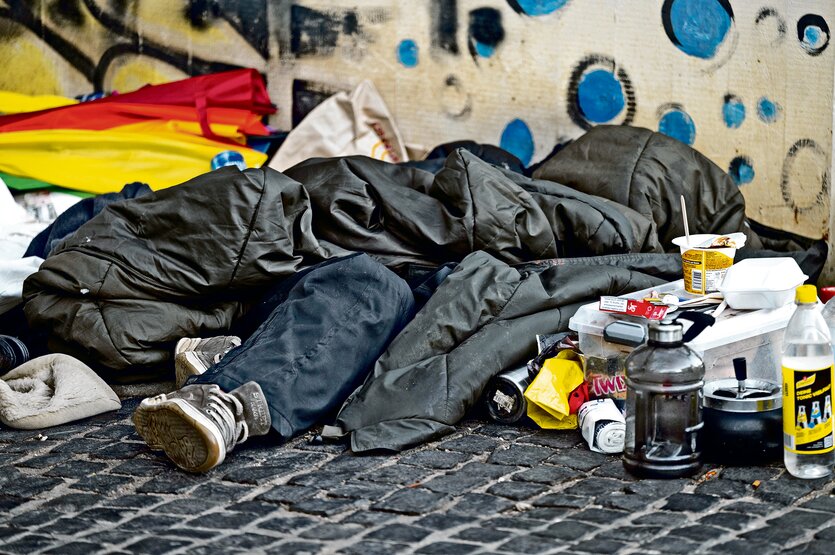 Obdachlose liegen unter Schlafsäcken auf dem Straßenpflaster.