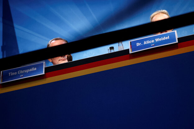 Alice Weidel und Tino Chrupalla sitzen auf einer blauen Pressetribüne, ihre Gesichter werden durch ein Absperrband verdeckt