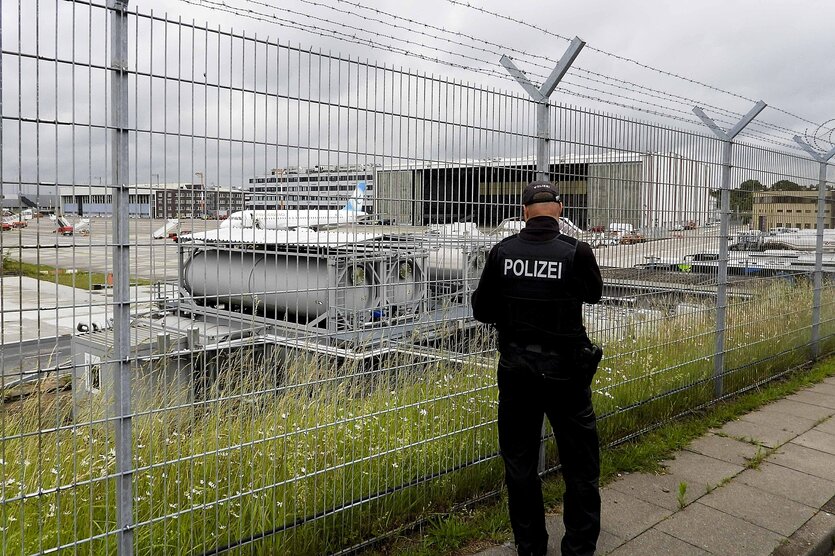 Ein Polizist steht vor der Umzäunung des Flugfeldes eines Flughafens