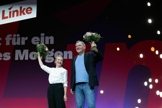 Ines Schwerdtner und Jan van Aken stehen mit Blumensträußen auf der Bühne