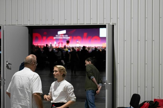 Ines Schwerdtner unterhält sich vor einer geöffneten Tür vor dem Saal mit einem Delegierten auf dem Bundesparteitag der Partei Die Linke in Halle/Saale. Hinter der Tür sieht man den Slogan 