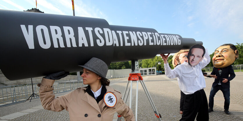 Menschen mit überdimensioniertem Fernrohr, auf dem "Vorratsdatenspeicherung" steht, einer ist maskiert als Justizminister Maas