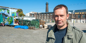 Ein Mann in einer grünen Jacke steht vor einem Industriegelände