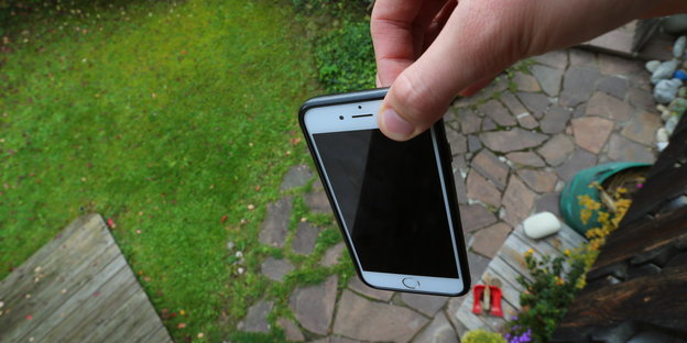 Mit zwei Fingern gehaltenes Smartphone über Abgrund
