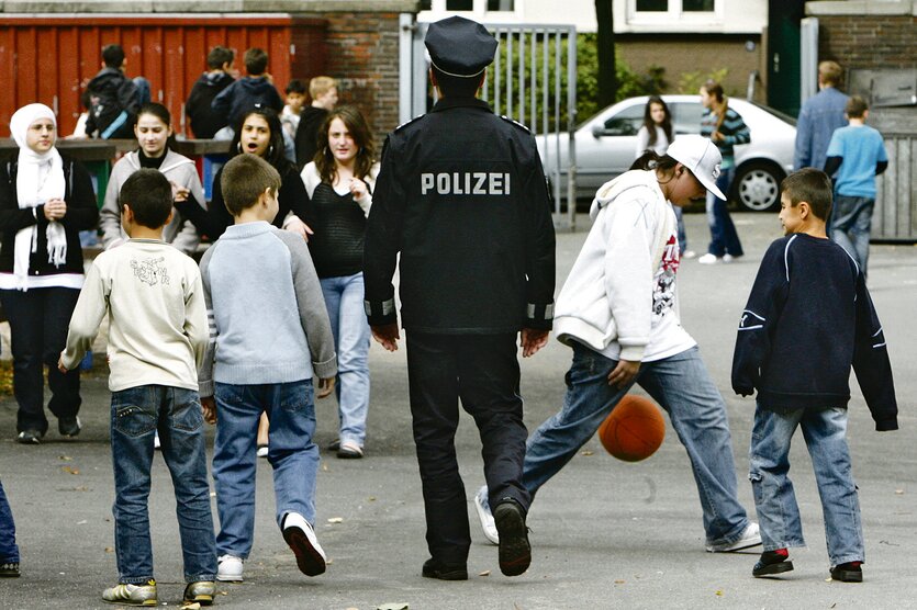 Ein Polizist in dunkler Jacke steht mit Kindern auf einem Schulhof