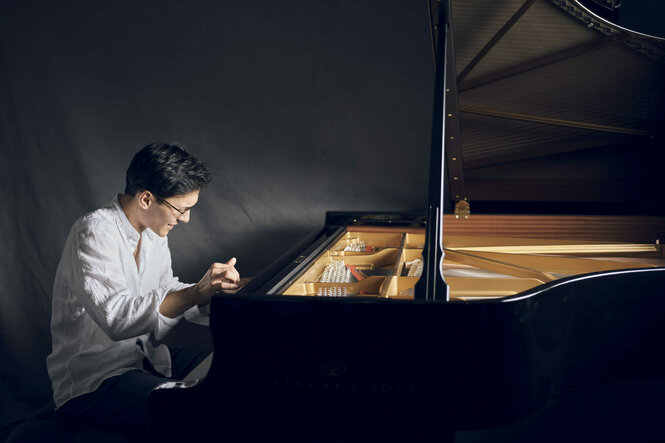 Der Pianist Nuron Mukumi sitz an einem aufgeklappten Flügel. Er trägt ein weißes Hemd und greift mit der linke Hand nach den Tasten