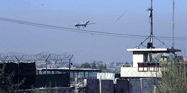 Mauern mit Stacheldraht und Sandsäcken im Vordergrund, hinten fliegt eine Drohne